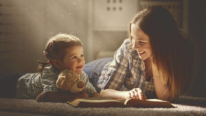 happy family mother and daughter read a book in the evening at home